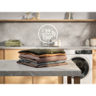 Harmaalla pöydällä on pino erilaisia taiteltuja vaatteita, taustalla näkyvät pesukone ja keittiöhylly.